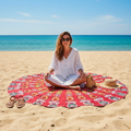 Woman sitting on Red Mandala Beach Throw Blanket on golden sand at the beach