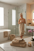 Woman wrapped in beige 700 GSM combed cotton bath towel in luxury marble bathroom