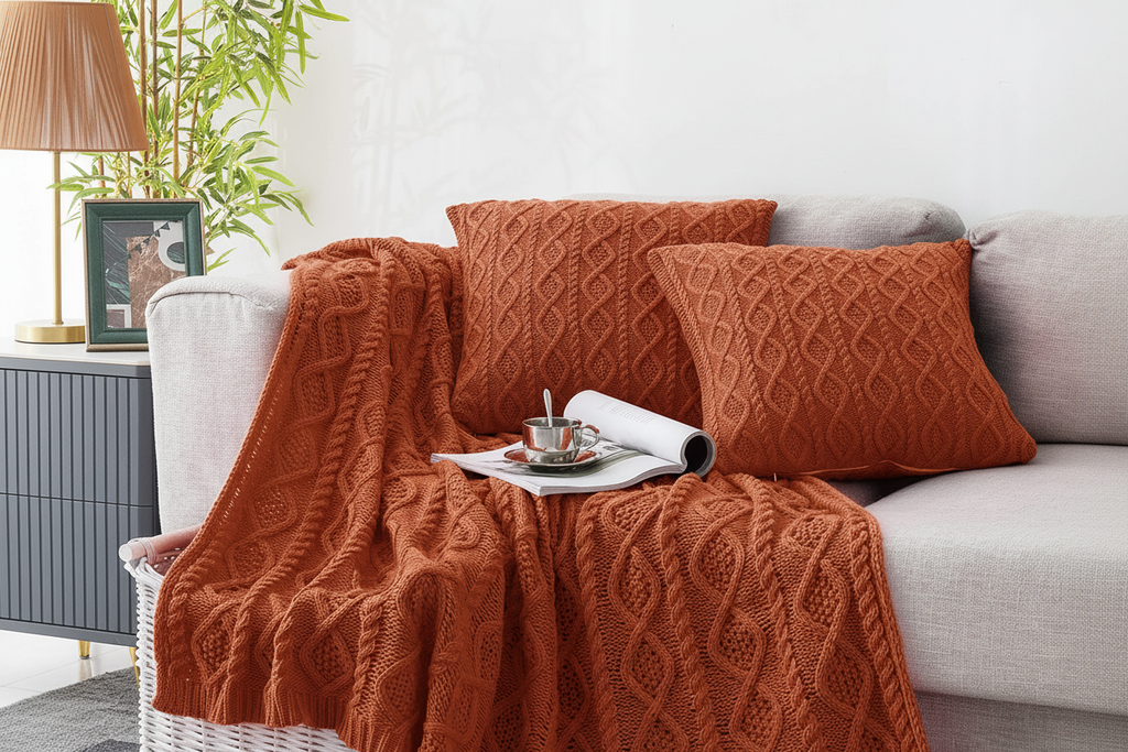 Rust cable knit throw blanket draped over a grey sofa with two matching cushion covers